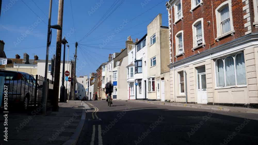 Rear view of unidentified bicycle rider passing camera point of view on East Street in Weymouth town, England. Rear view of unidentified bicycle rider passing camera point of view on East Street in Weymouth town, England.