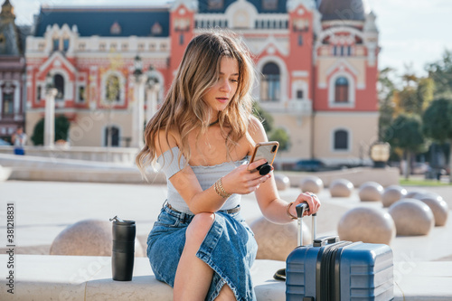 Young woman carrying her suitcase and using her smartphone photo