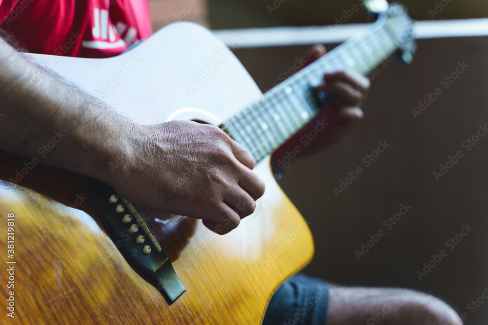 Fototapeta premium Detail of midsection of man with acoustical guitar focus on hand unknown person playing - shallow depth of field music instrument leisure concept