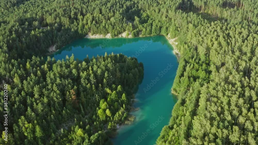Aerial top view amazing blue lake surrounded by green pine forest. Curved lakeshore and clear turquoise water. Pond in woodland. Golden hour, warm sunlight during sunset or sunrise Aerial top view amazing blue lake surrounded by green pine forest. Curved lakeshore and clear turquoise water. Pond in woodland. Golden hour, warm sunlight during sunset or sunrise