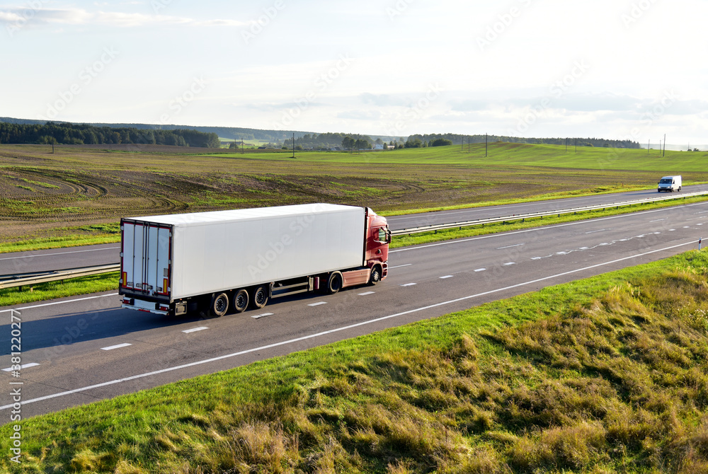 White truck with semi-trailer driving along highway on the sunset background. Goods delivery by roads. Services and Transport logistics. 