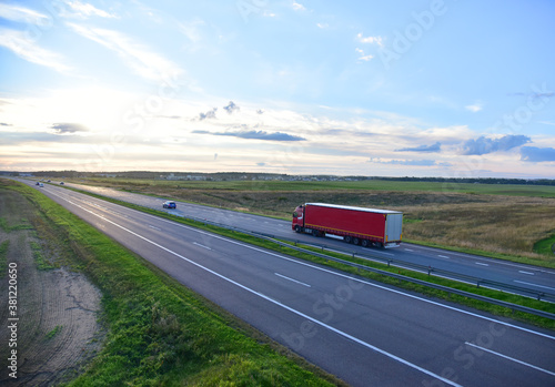 Red truck with semi-trailer driving along highway on the sunset background. Goods delivery by roads. Services and Transport logistics. 
