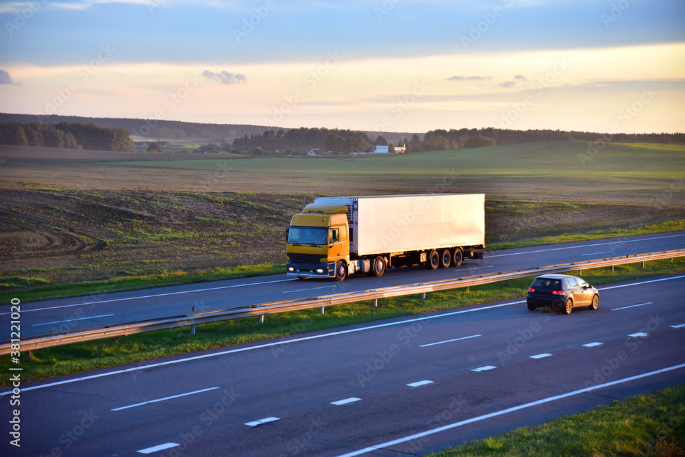 Truck with semi-trailer driving along highway on the sunset background. Goods delivery by roads. Services and Transport logistics.