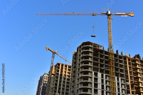 Tower cranes in action on blue sky background. Construction of new multi-storey buildings. Residential building is being constructed use of crane. Pouring of concrete in formwork