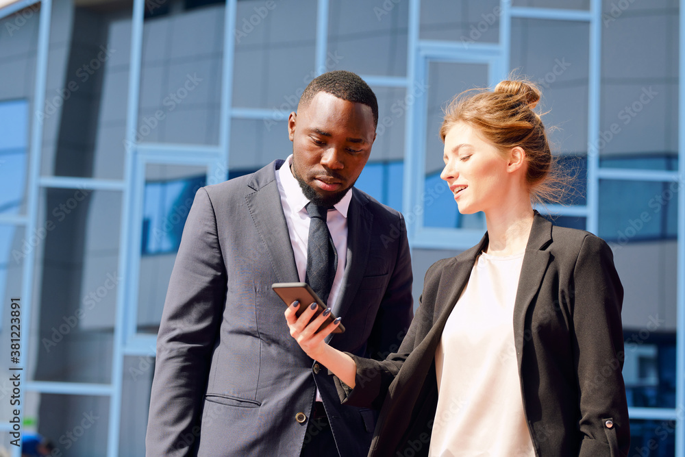 Young businesswoman with smartphone showing her colleague timetable of flights Young businesswoman with smartphone showing her colleague timetable of flights