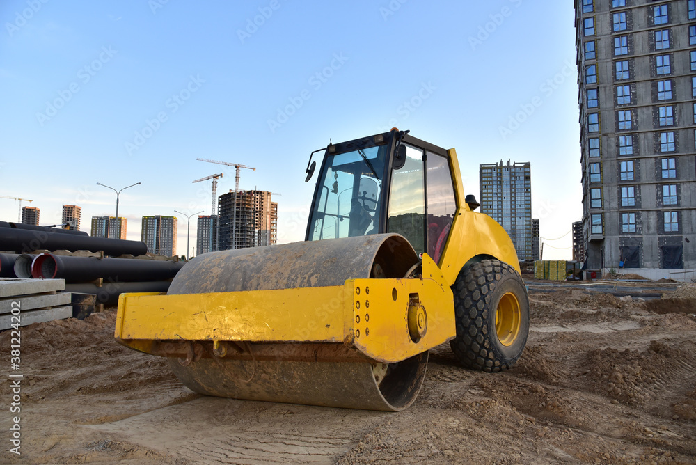 Vibro Roller Soil Compactor leveling ground at construction site. Vibration single-cylinder road roller on construction road. Road work for new asphalt laying. Tower cranes build high-rise buildings