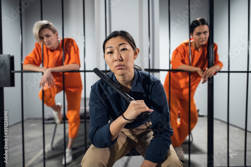 Portrait of an asian security guard against the background of two cute criminals in the cells. © Anna Kosolapova