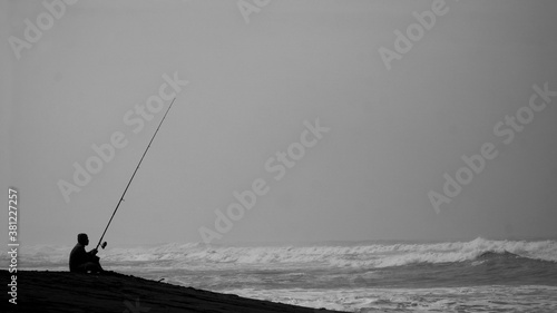 Silhouette of man fishing by the sea. Sitting alone holding the long fishing rod.