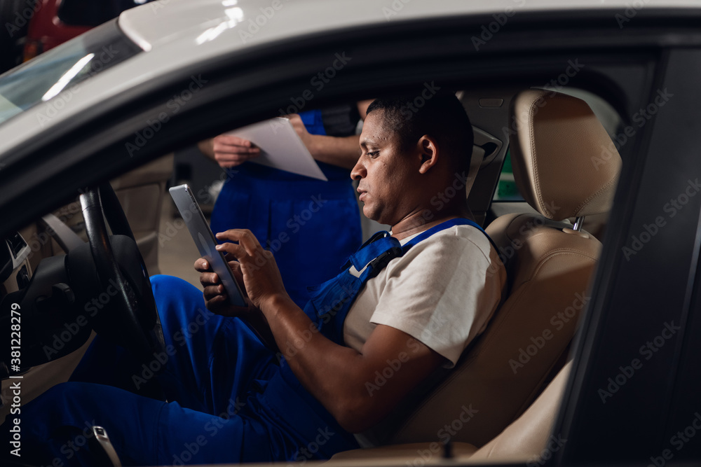Two repairmen inspect the car inside and use the tablet Two repairmen inspect the car inside and use the tablet