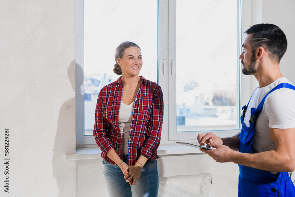 Fototapeta premium A repairman in a blue overalls shows the woman the renovation of an apartment. He writes notes with a pen