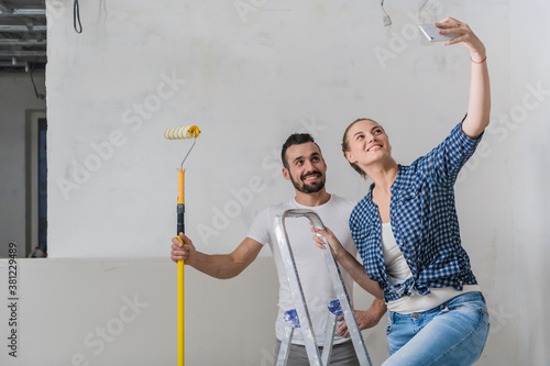 Married couple taking selfie on the background of the wall with a stepladder and roller