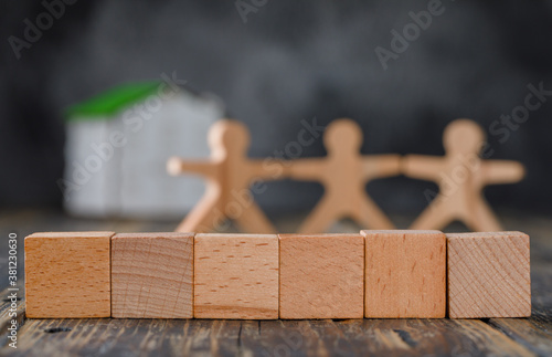 Family safety concept with wooden figures of people, cubes, model house on wooden and foggy background side view.