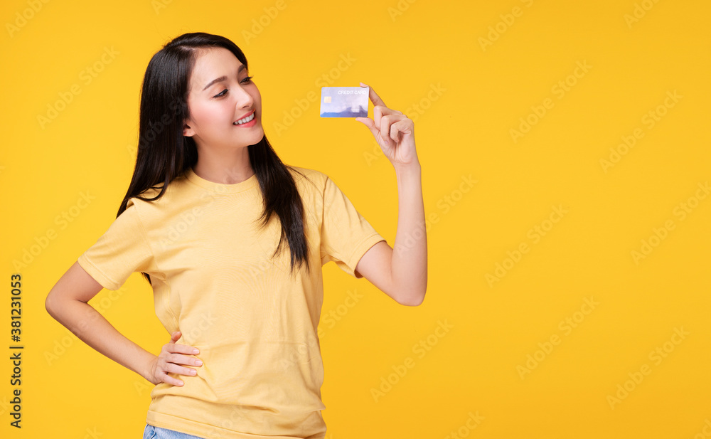 Cheerful asian woman wearing casual clothes while holding and looking to credit card mockup in hand over isolated white background. Payment purchase and financial concept. Cheerful asian woman wearing casual clothes while holding and looking to credit card mockup in hand over isolated white background. Payment purchase and financial concept.