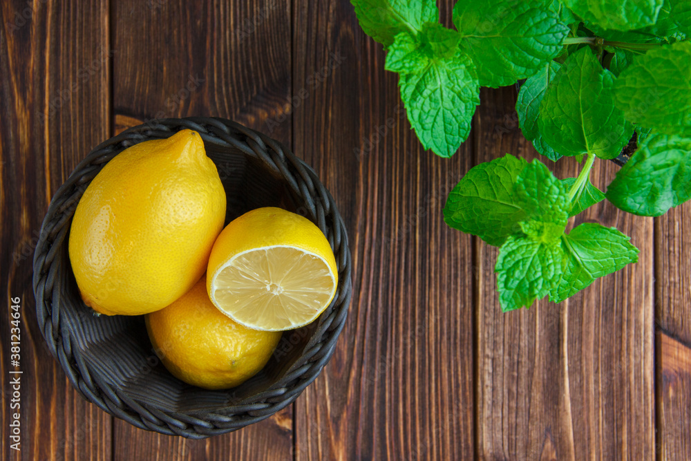 Lemons with herbs in a wicker basket on wooden background, flat lay.