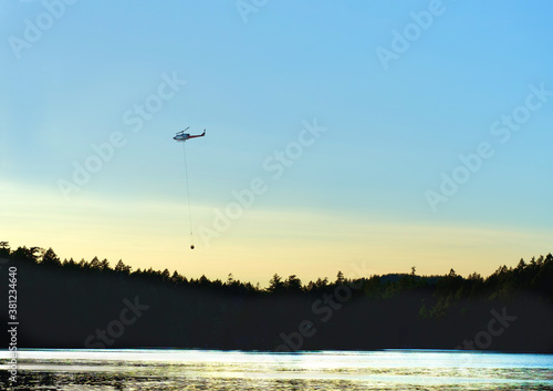 Water bomber helicopter lifting water out of a lake at sunset