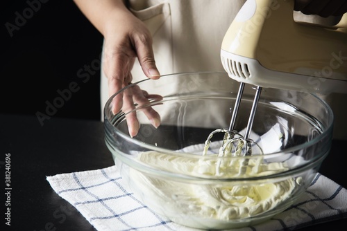 Lady is making cream cake using electric portable mixer machine photo