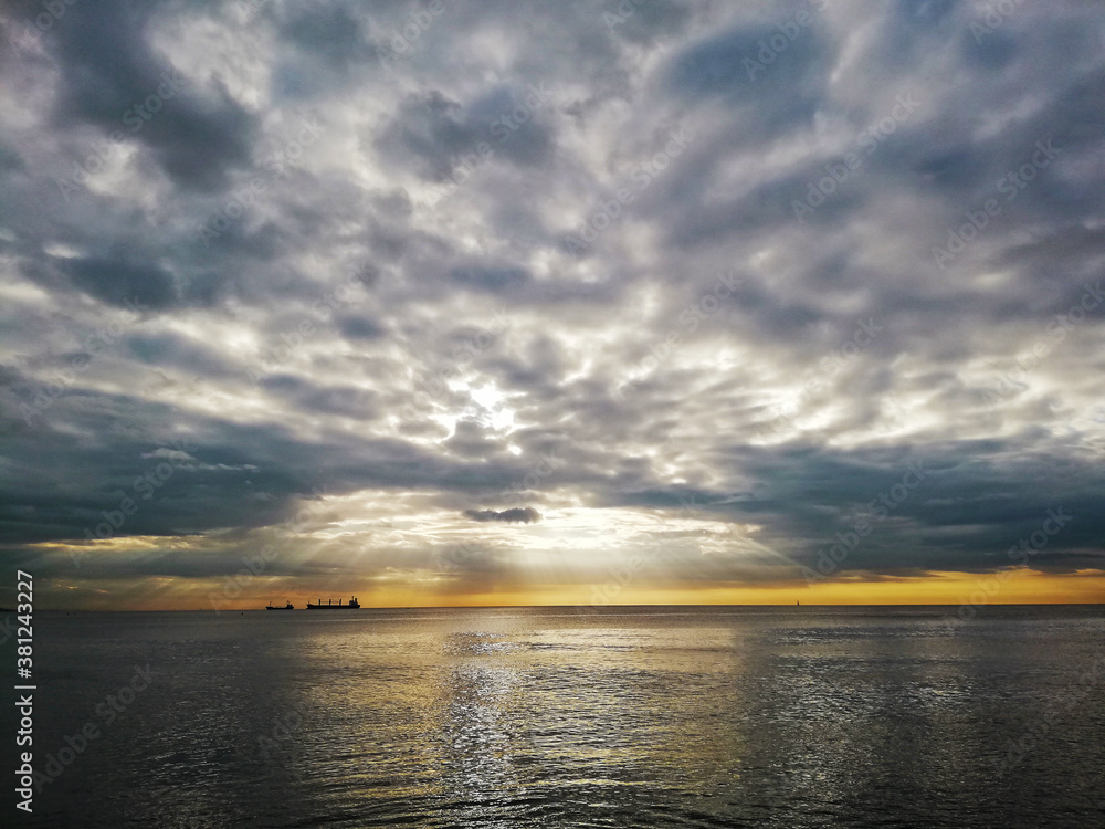 Beautiful cloudy sunset in the Caribbean Sea, the sunset produces yellow and orange colors, cargo ships are seen on the horizon.