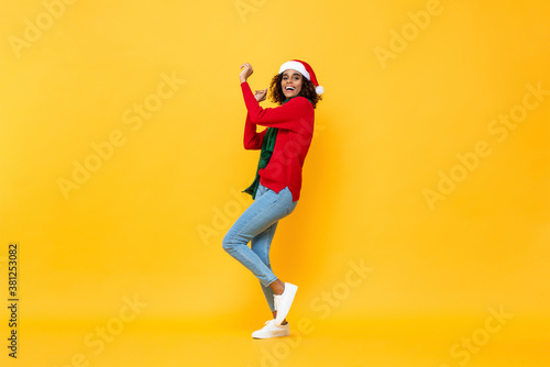 Full length portrait of fun happy woman in Christmas attire dancing on isolated yellow studio background © Atstock Productions