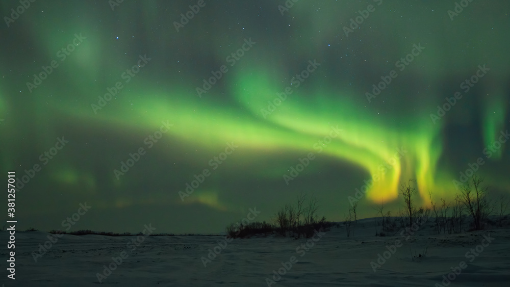 Aurora over a frozen river and snow-covered tundra. Night arctic landscape. Northern lights and stars in the night sky. Amazing northern nature of Chukotka and polar Siberia. Far North of Russia.
