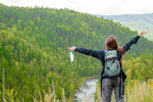 Happy woman holds face mask at mountains after ending coronavirus and flu outbreak. Back view