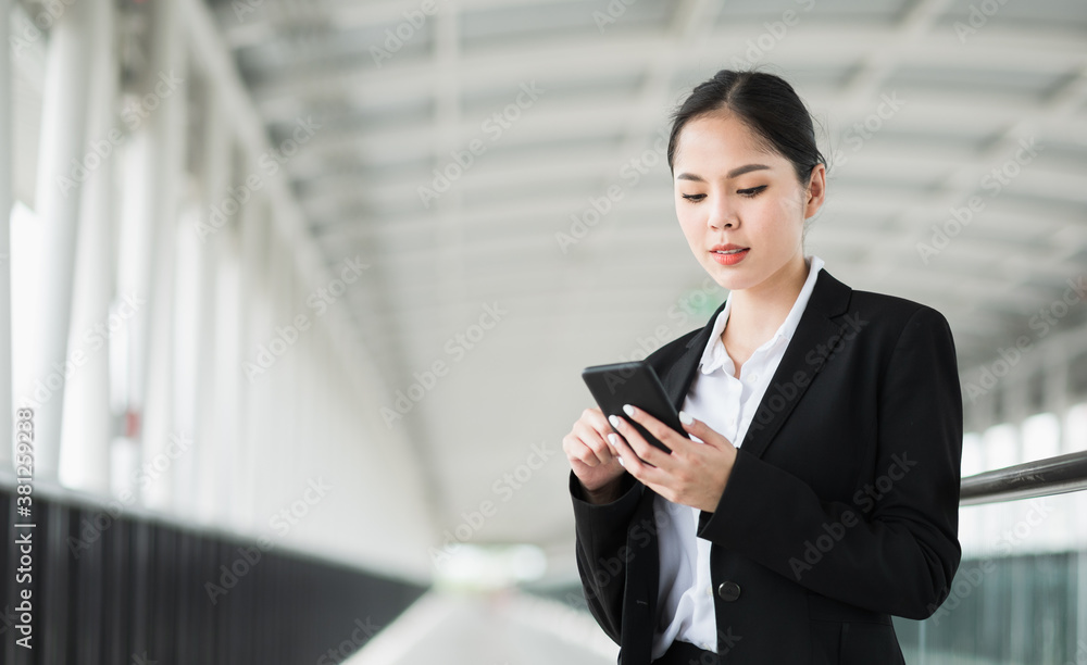Young asian business woman sitting on trolley and using smartphone. Beautiful female in black suited. Young asian business woman sitting on trolley and using smartphone. Beautiful female in black suited.