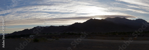 Sunset in the Andes mountains. Panorama view of the dirt road and the sun hiding behind the dark mountains silhouette at dusk. 