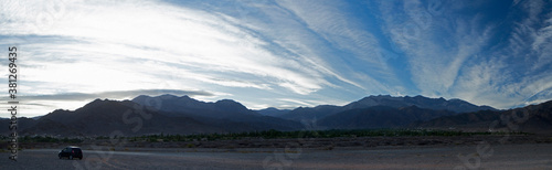 Travel. Panorama view of a car parked in the dirt road across the desert and mountains under a beautiful sunrise blue sky.