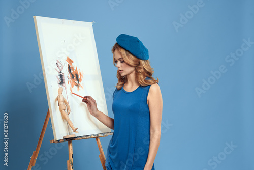 Woman artist paintbrush paint on canvas easel art education blue background