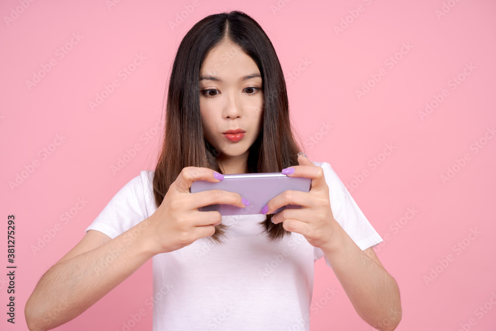 Asian woman playing games on mobile phones on a pink background. Asian woman playing games on mobile phones on a pink background.