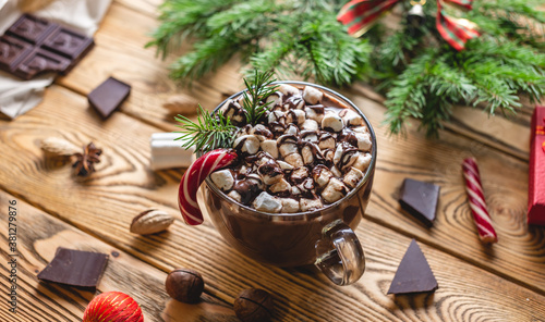 A cup of aromatic tasty hot chocolate with marshmallows decorated with red candy on a wooden table surrounded by Christmas accessories. Concept of a festive atmosphere and cozy New Year mood