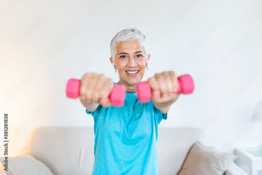 Senior woman exercising with dumbbells at home. Sporty beautiful woman exercising at home to stay fit. Elderly woman exercising at home. Fitness, workout, healthy living and diet concept.
