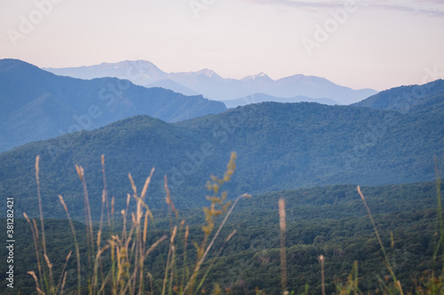 Early morning just after sunrise. Silhouettes of mountains in the morning haze, grass and wildflowers in the foreground. Alpine summer landscape. Lagonaki Plateau, Republic of Adygea, Russia