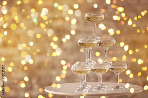 Tower made of glasses with champagne on table against blurred lights