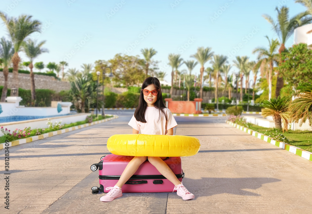 Cute girl with suitcase and inflatable ring at tropical resort