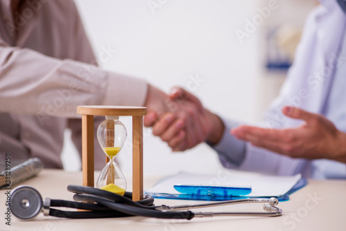 Old male patient visiting young doctor in time management concep photo