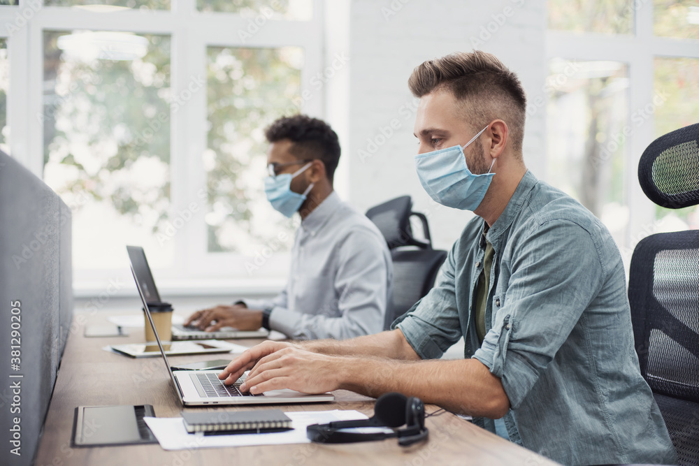Young people professionals working in office wearing medical protective masks - Colleagues using laptops in coworking - Selfcare, coronavirus COVID-19 protection, social distancing, healthcare concept Young people professionals working in office wearing medical protective masks - Colleagues using laptops in coworking - Selfcare, coronavirus COVID-19 protection, social distancing, healthcare concept