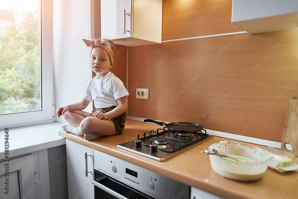 Little girl makes dough on kitchen.