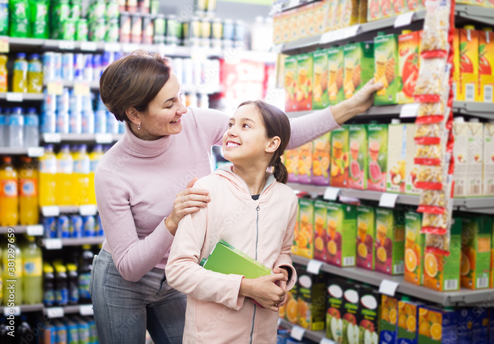 satisfied woman with daughter choosing refreshing beverages on shelves in supermarket