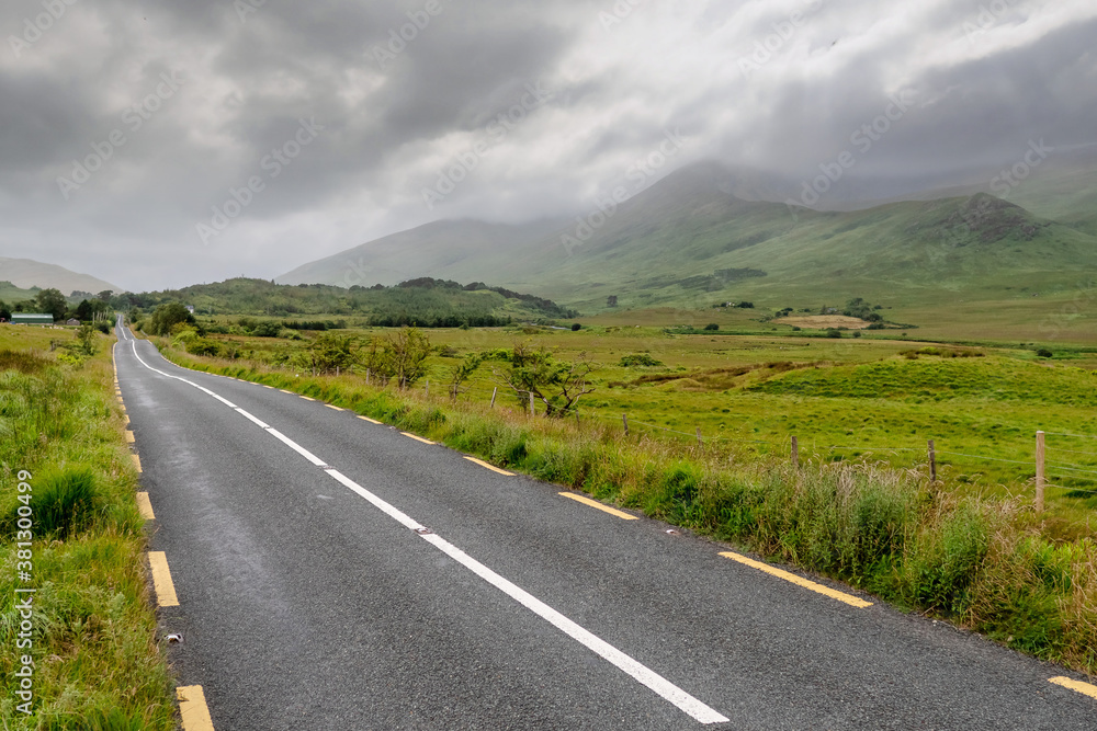 Small narrow road without hard shoulder in Connemara, Ireland, Mountains covered with low cloudy sky. Nobody.
