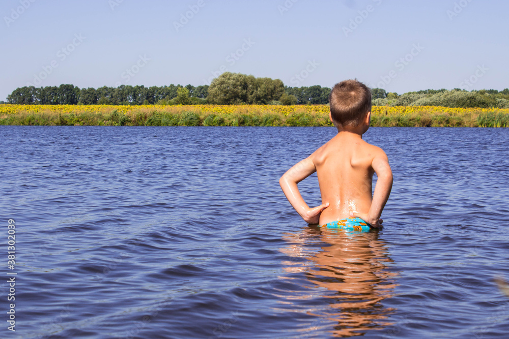 a boy stands in a river against the background of a yellow field a boy stands in a river against the background of a yellow field