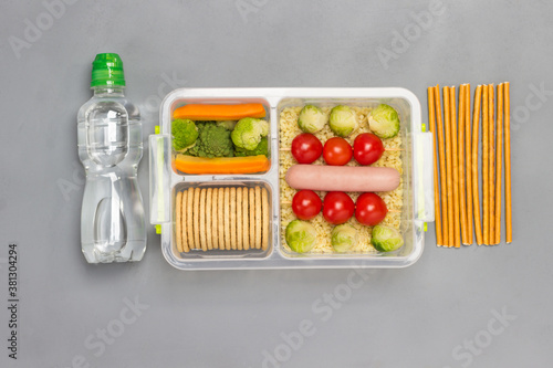 Lunch box with sausage, broccoli and tomatoes. Bottle of water and edible straw
