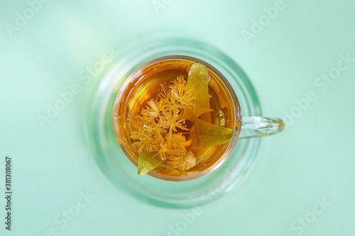 A cup of freshly brewed tea with  linden flowers on a green background, top view.