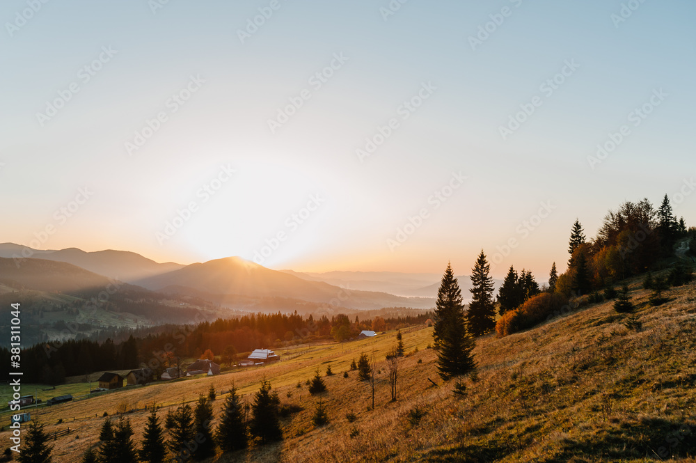 Autumn afternoon in the mountains. Trees on the edge of a hill in fall colors. The wonderful countryside in the morning. Amazing view on a sunny autumn day with fog and high mountain peaks behind.