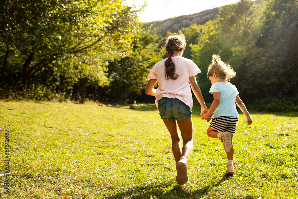 Fototapeta premium Two sisters run hand in hand on the green grass. Children play in nature. 