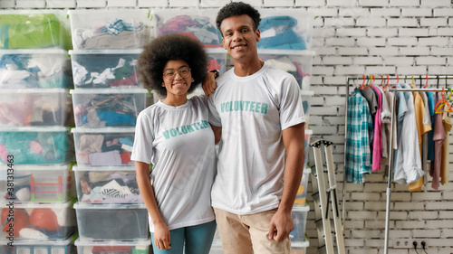 Photos Two young diverse volunteers smiling at camera, posing together in front of rack