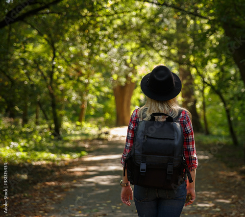 young caucasian girl travels in a hat and with a backpack through the forest or park in the shade of trees .background blurred.  © Margo_Alexa