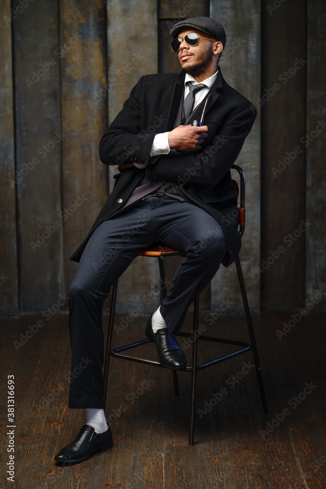 Studio shot of stylish african american man wearing coat, cap, glasses and holding smoking pipe Studio shot of stylish african american man wearing coat, cap, glasses and holding smoking pipe
