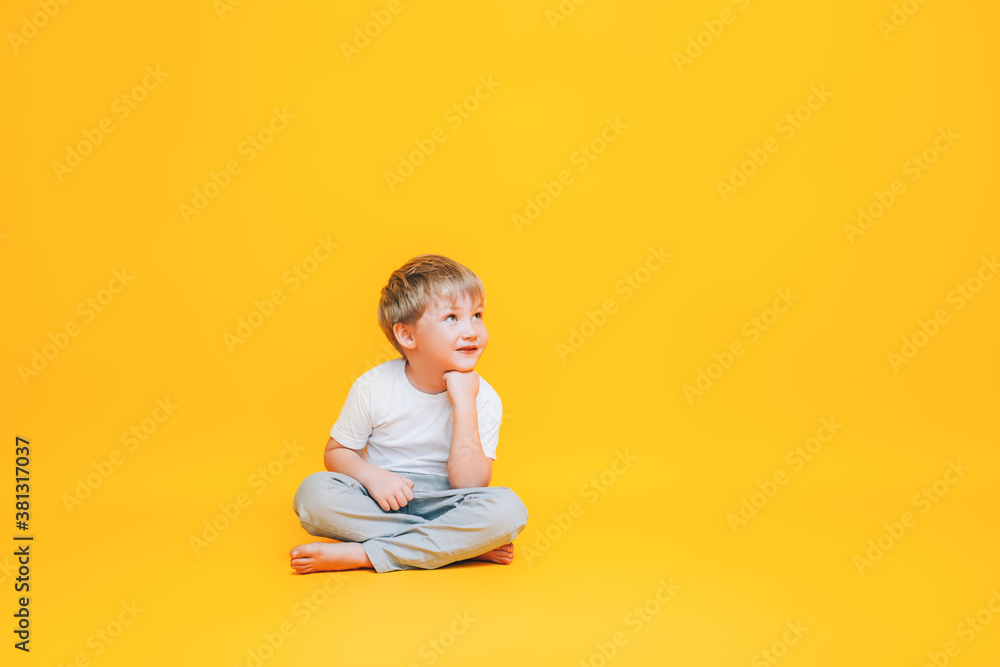 Pensive little boy in white t-shirt sitting on yellow background Pensive little boy in white t-shirt sitting on yellow background