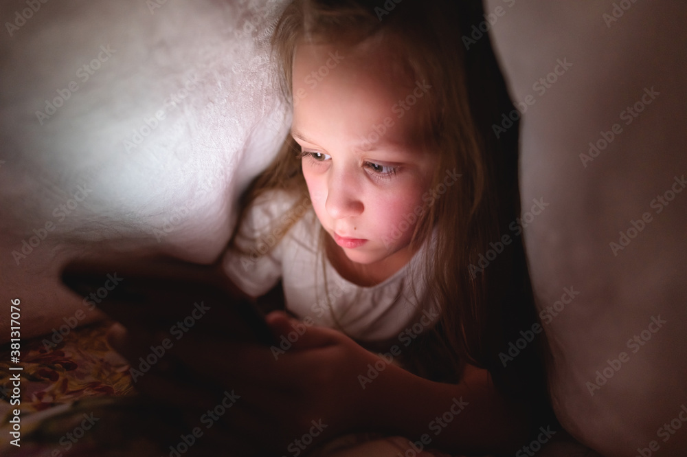 Little girl at night with a smartphone under the covers. Childhood gadget addiction and insomnia Little girl at night with a smartphone under the covers. Childhood gadget addiction and insomnia
