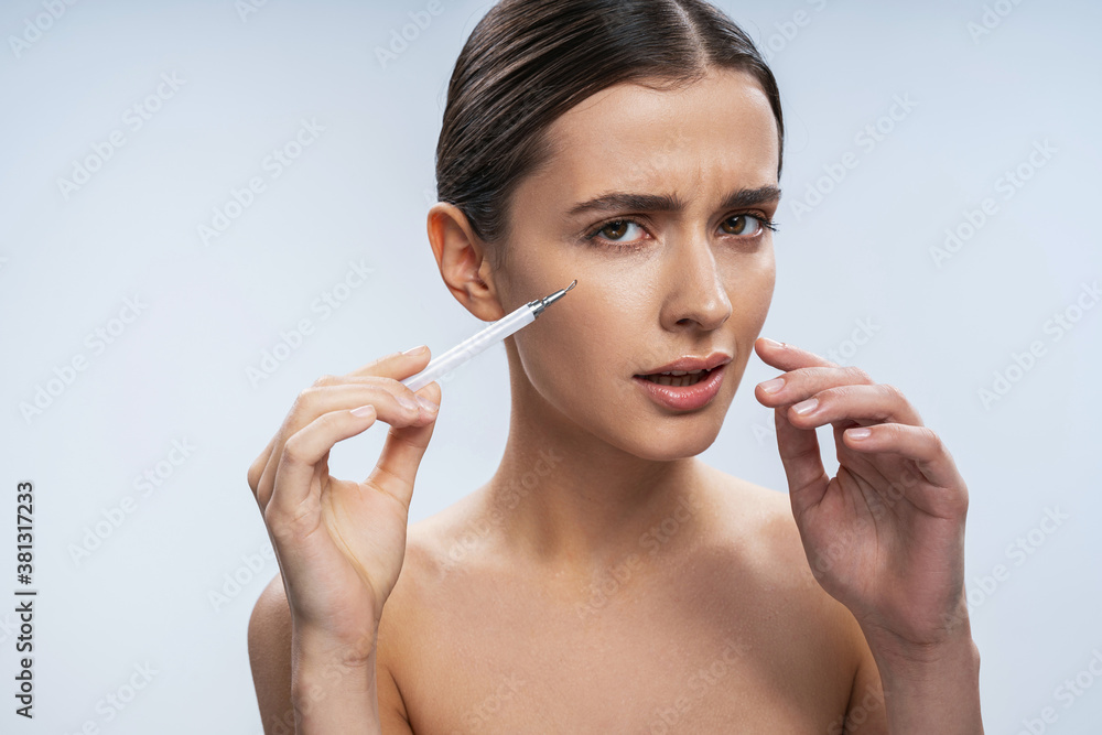 Beautiful woman feeling confused while receiving facial injection Beautiful woman feeling confused while receiving facial injection
